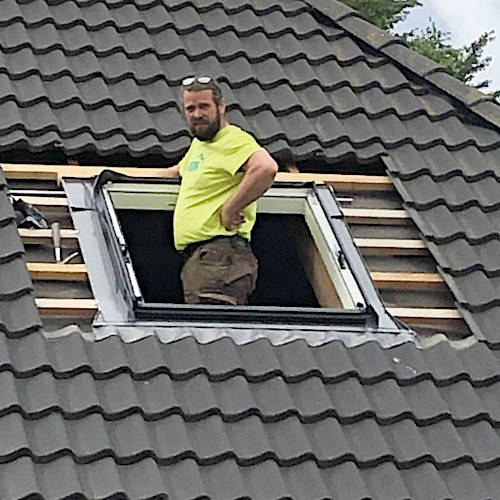 Lutz Kofalk steht im Dachfenster auf einem neu eingedeckten Dach